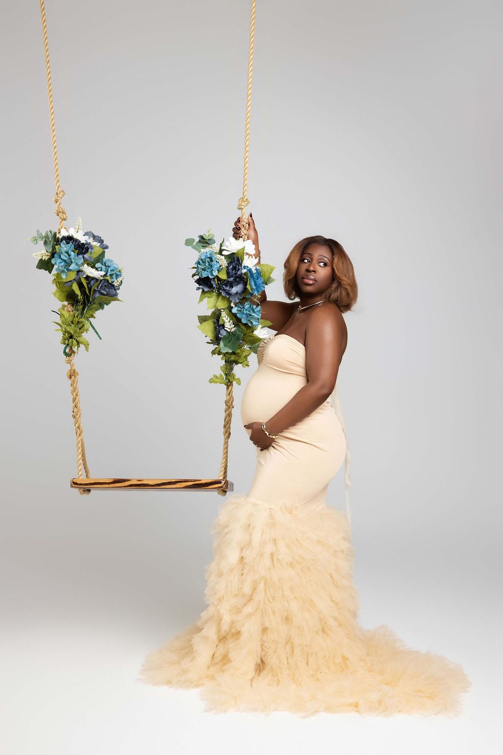Maternity portrait on a flower swing in a peach ruffled gown