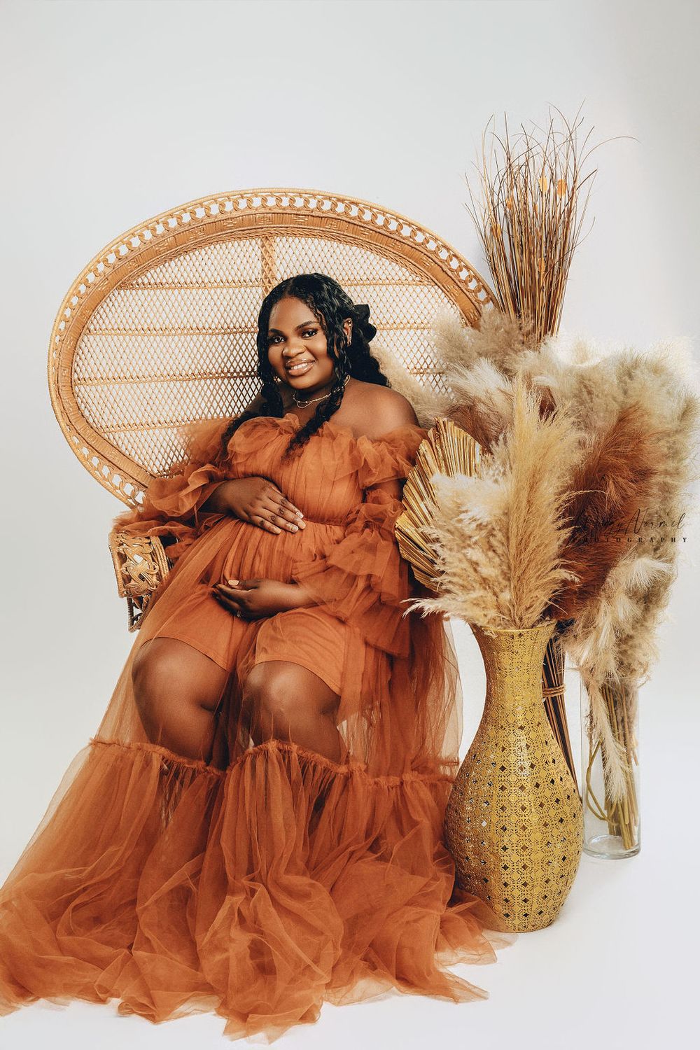 Expectant mother in a rust tulle gown against a soft green studio backdrop