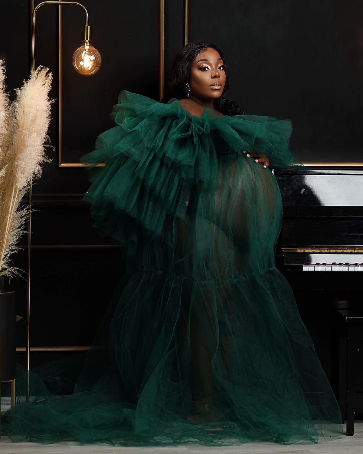 Maternity portrait in a deep green tulle gown beside a grand piano