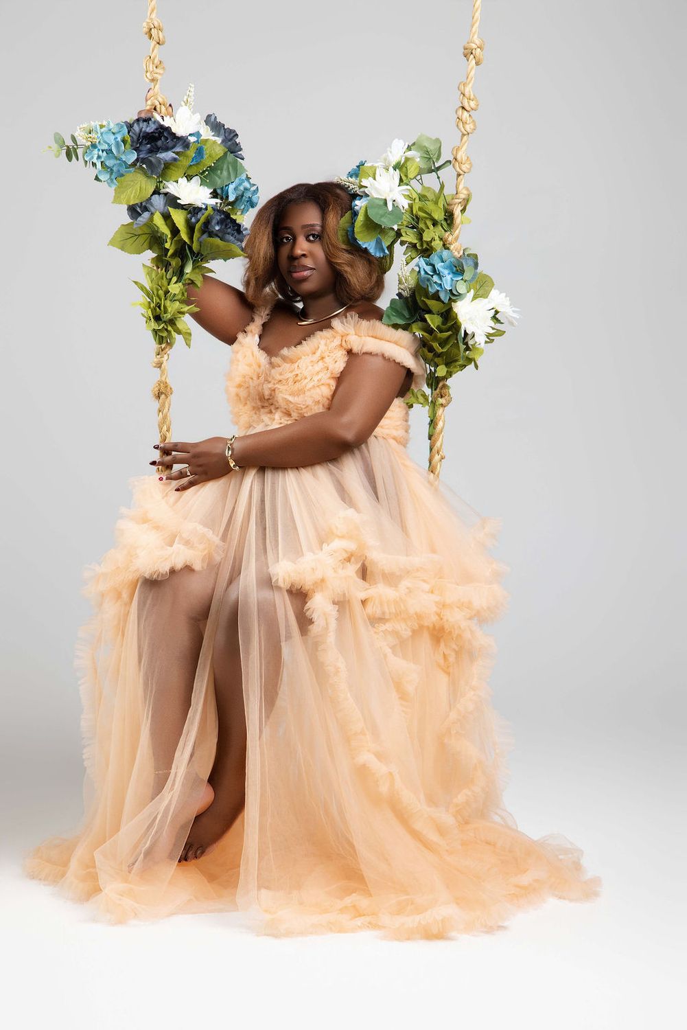 Mother to be seated on a flower swing in a peach gown, studio maternity session