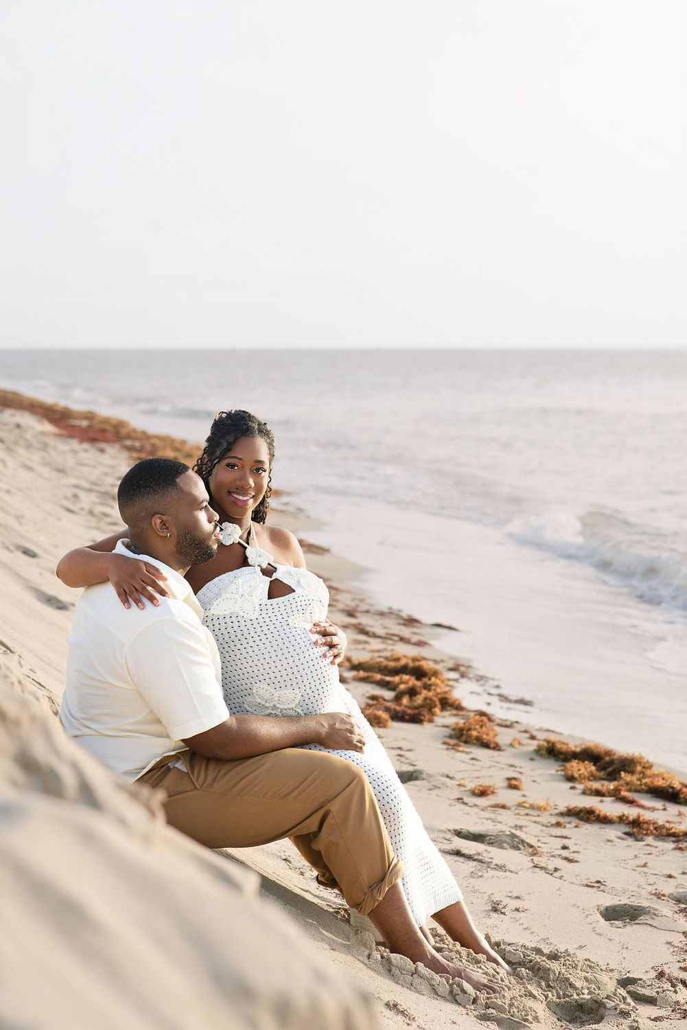Expecting couple sitting together in the sand as the light goes