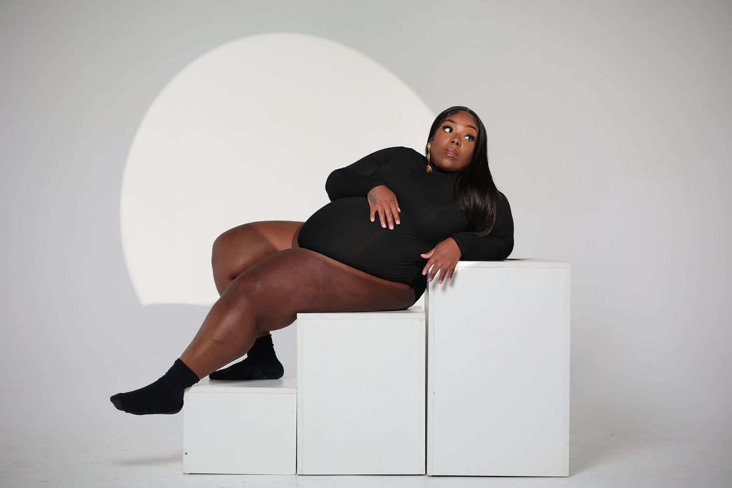 Editorial studio maternity portrait in black, lit by a single circular source