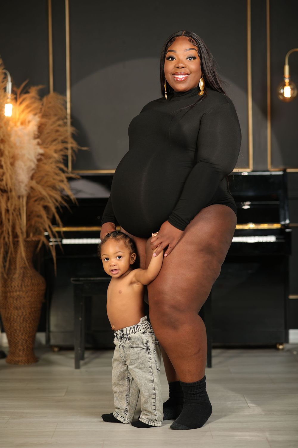 Expectant mother with her toddler beside a piano and pampas grass