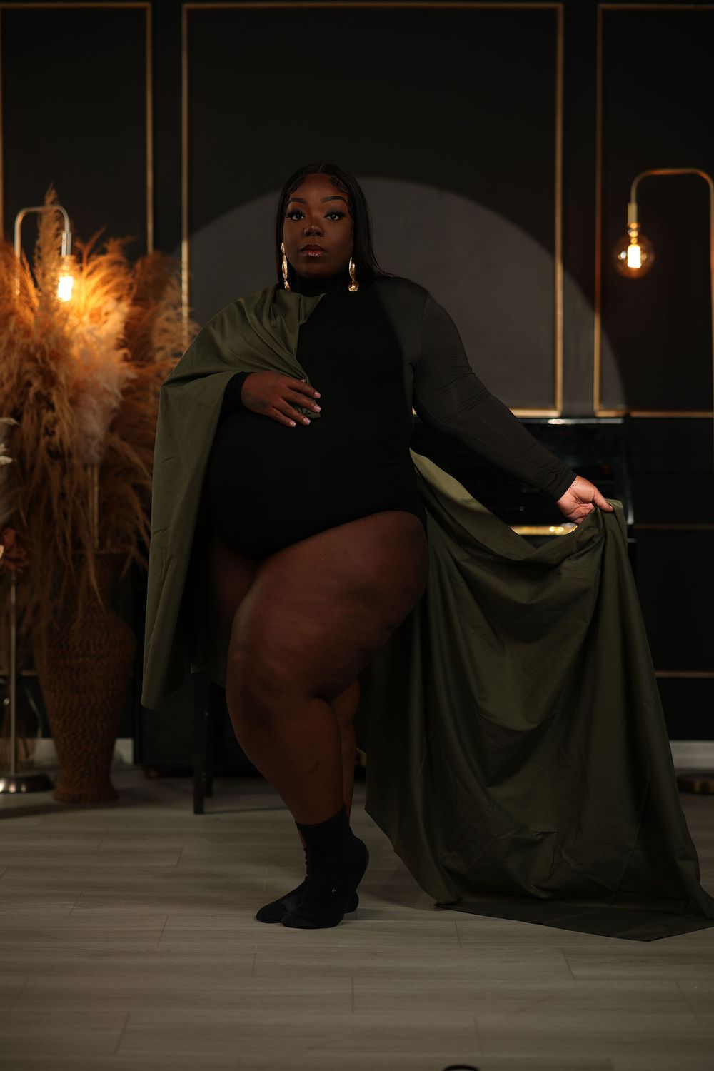 Expectant mother in profile wearing an olive cape in a dark studio