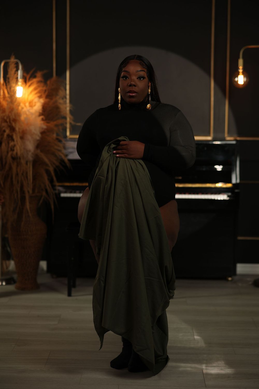 Mother to be with an olive cape falling behind her in a dark studio