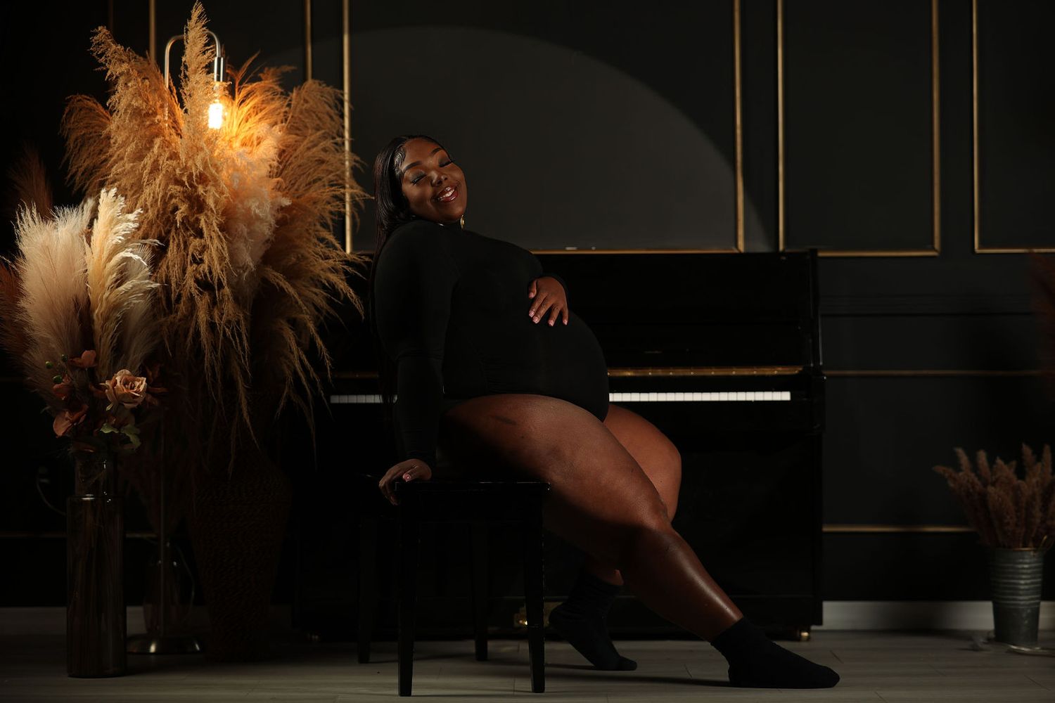 Mother to be seated among pampas grass in warm low studio light