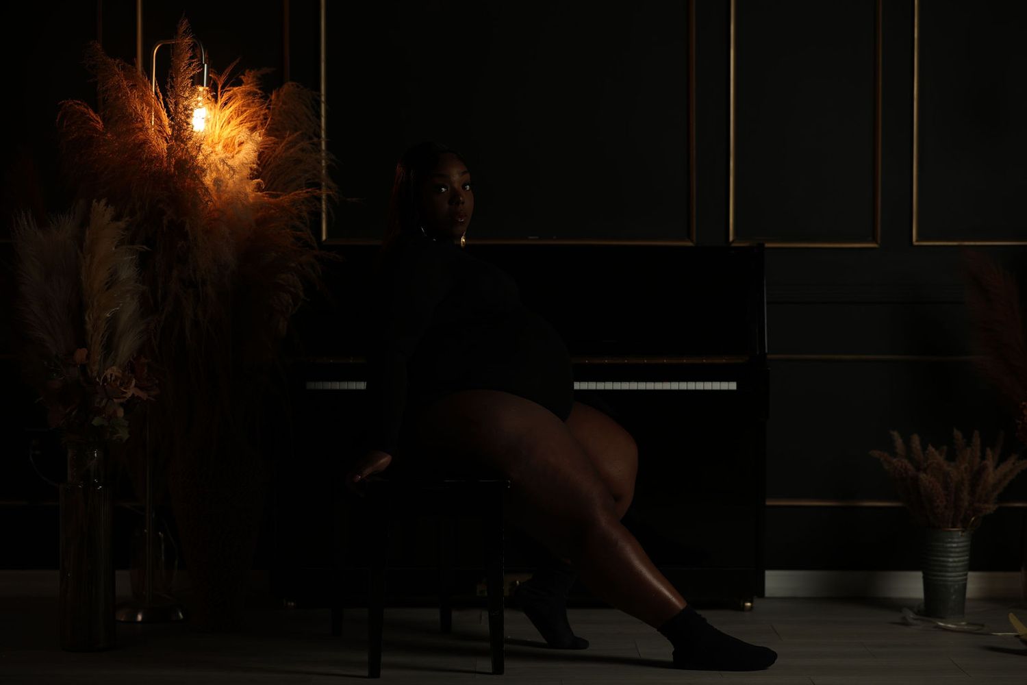 Expectant mother seated in warm light with pampas grass and a piano behind