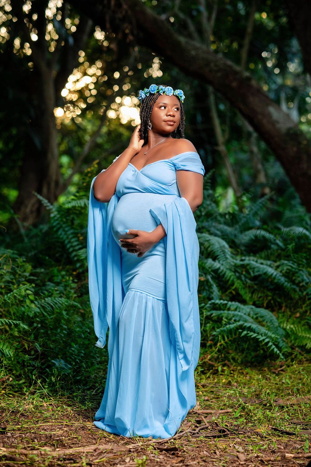 Expectant mother in a blue gown among tree ferns at dusk