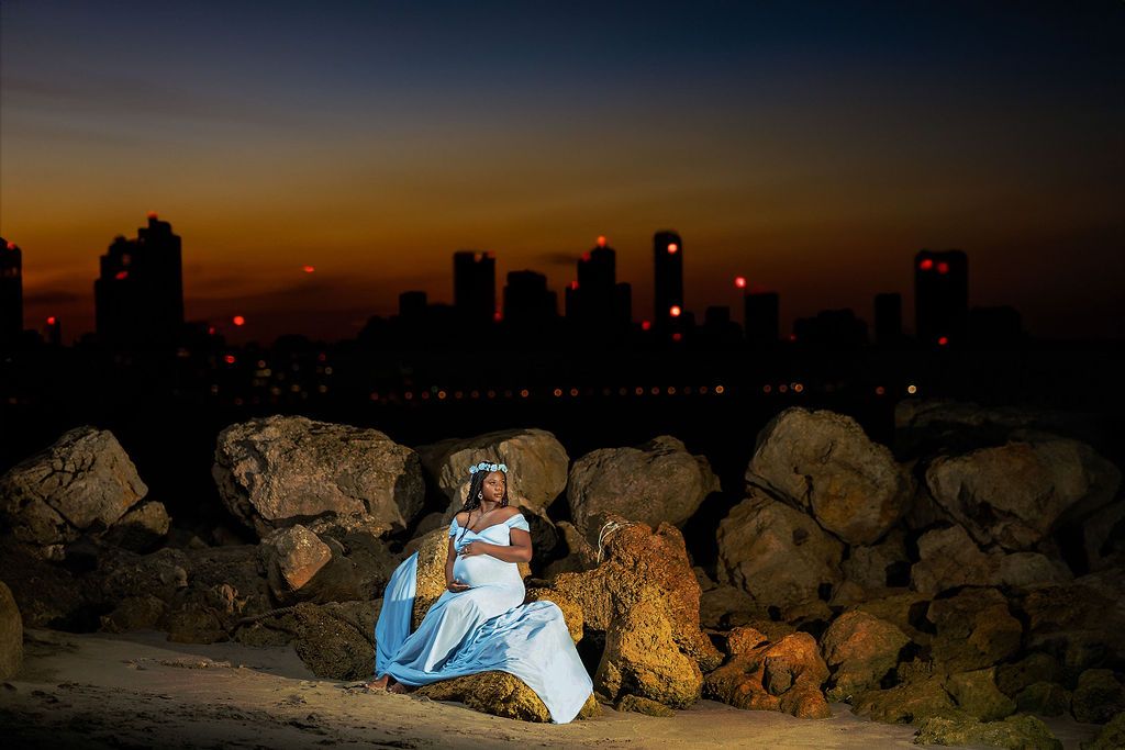 Expectant mother on the breakwater rocks with the Miami skyline burning behind her