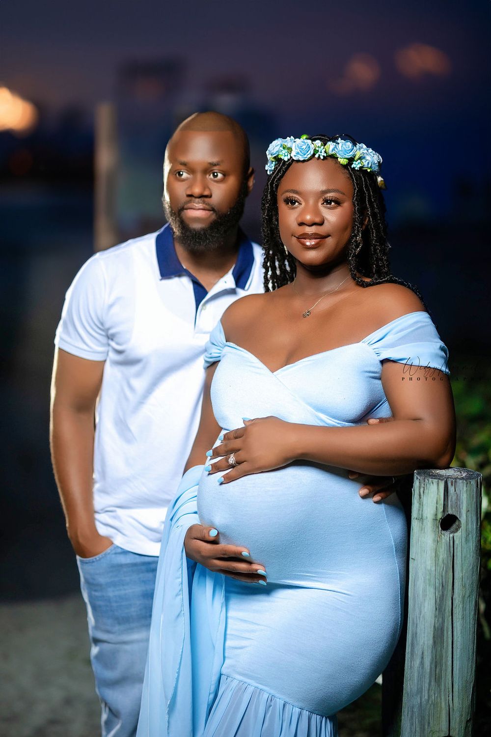 Expecting couple by the water at dusk, his hands on her belly