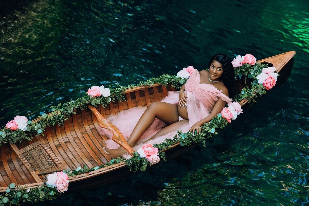 Expectant mother lying in a flower covered canoe on the hidden blue lagoon