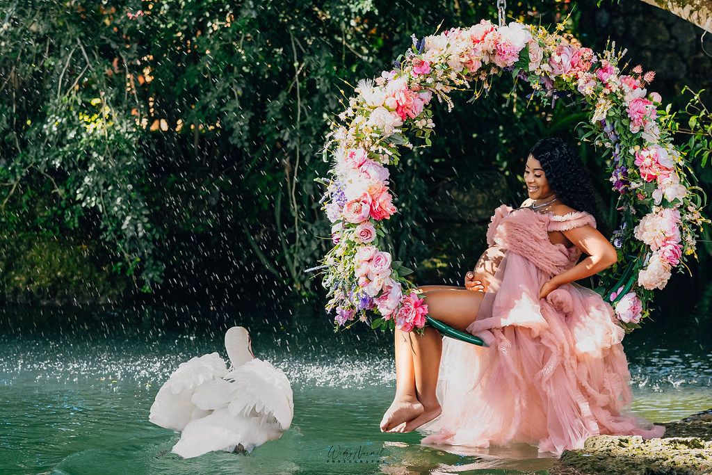 Expectant mother on a floral swing arch above the lagoon with a swan below