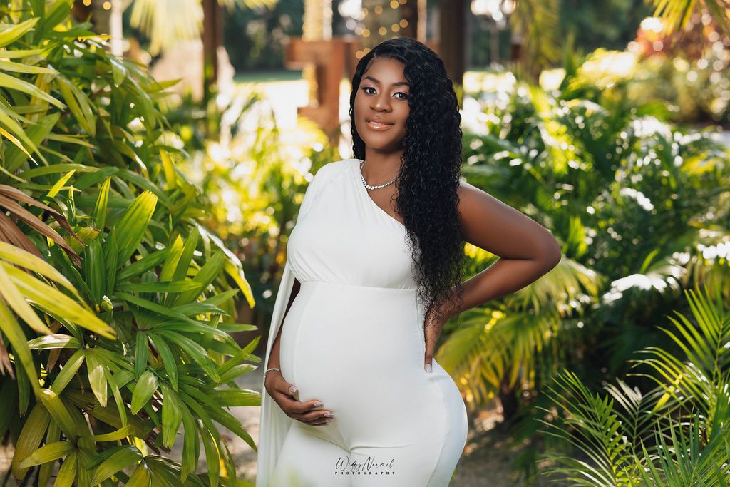 Mother to be in a fitted white gown surrounded by tropical foliage