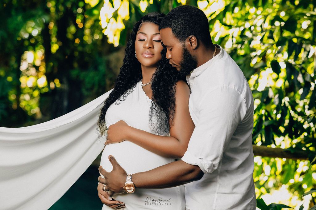 Expecting couple in white with fabric lifting behind them in a tropical garden