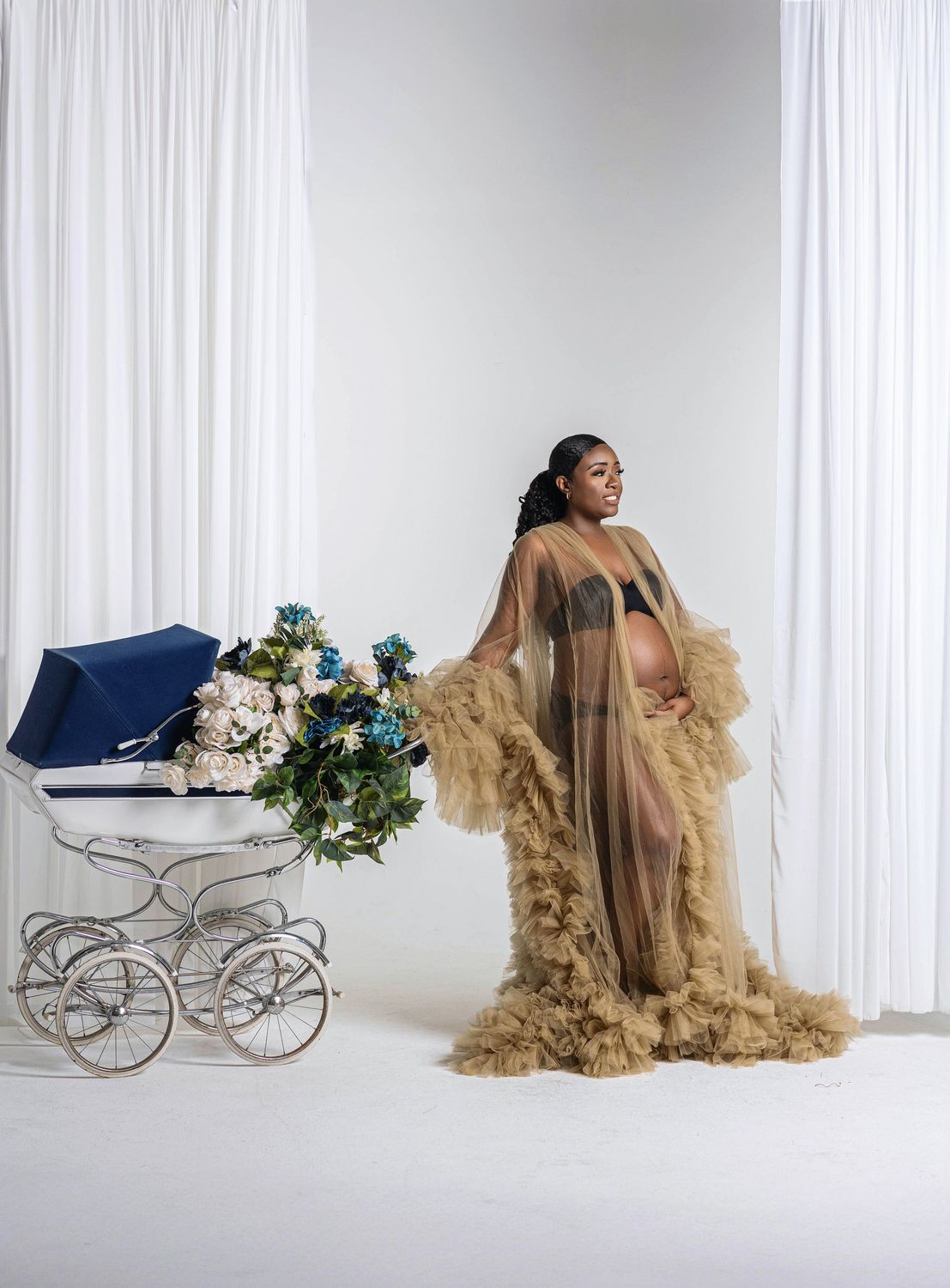 Expectant mother in a champagne tulle gown beside a vintage carriage