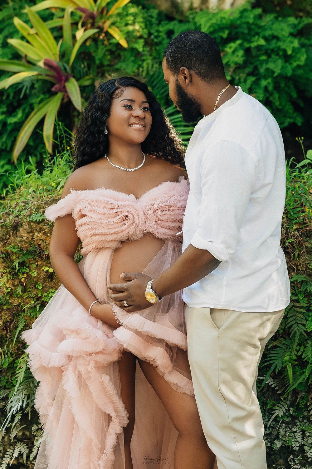 Expecting couple holding her belly together among the bromeliads