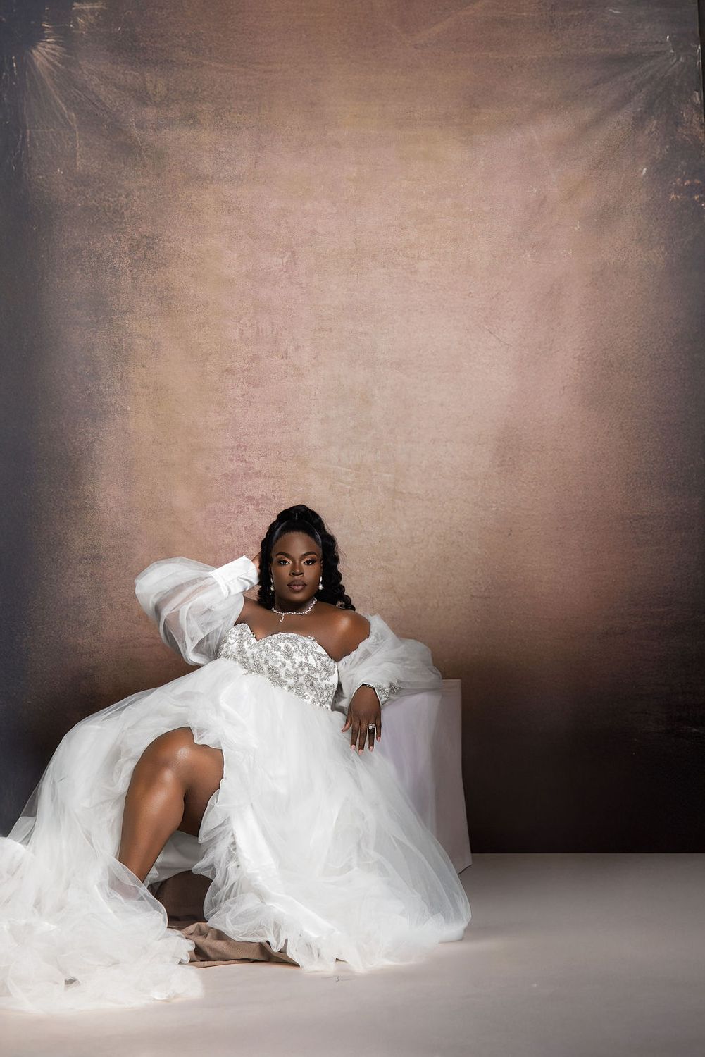 Expectant mother in white tulle against a warm painted backdrop