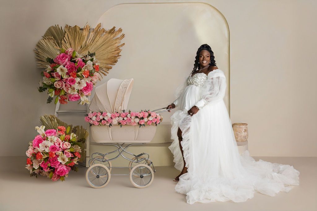 Mother to be in white tulle with a flower filled pram and dried palms