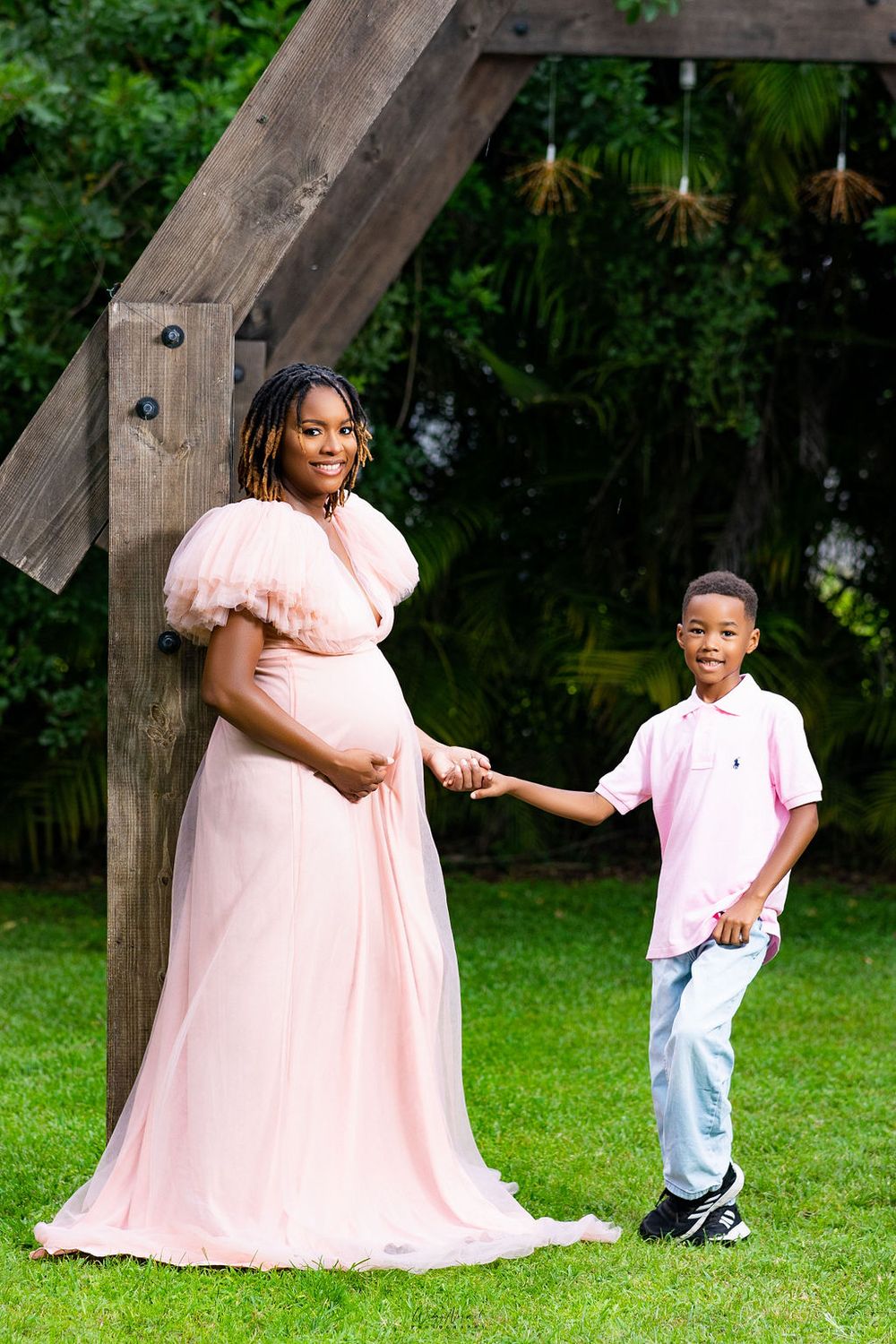 Mother to be holding her son's hand on the lawn, both in blush and pink