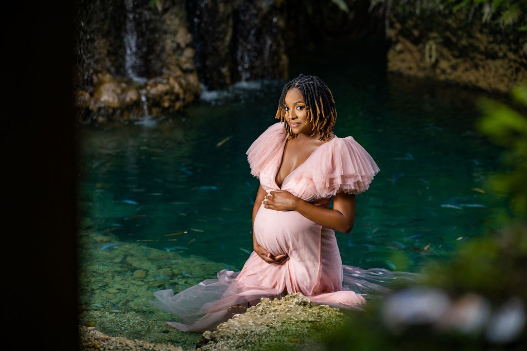 Mother to be in blush at the edge of the dark spring, light falling through the canopy
