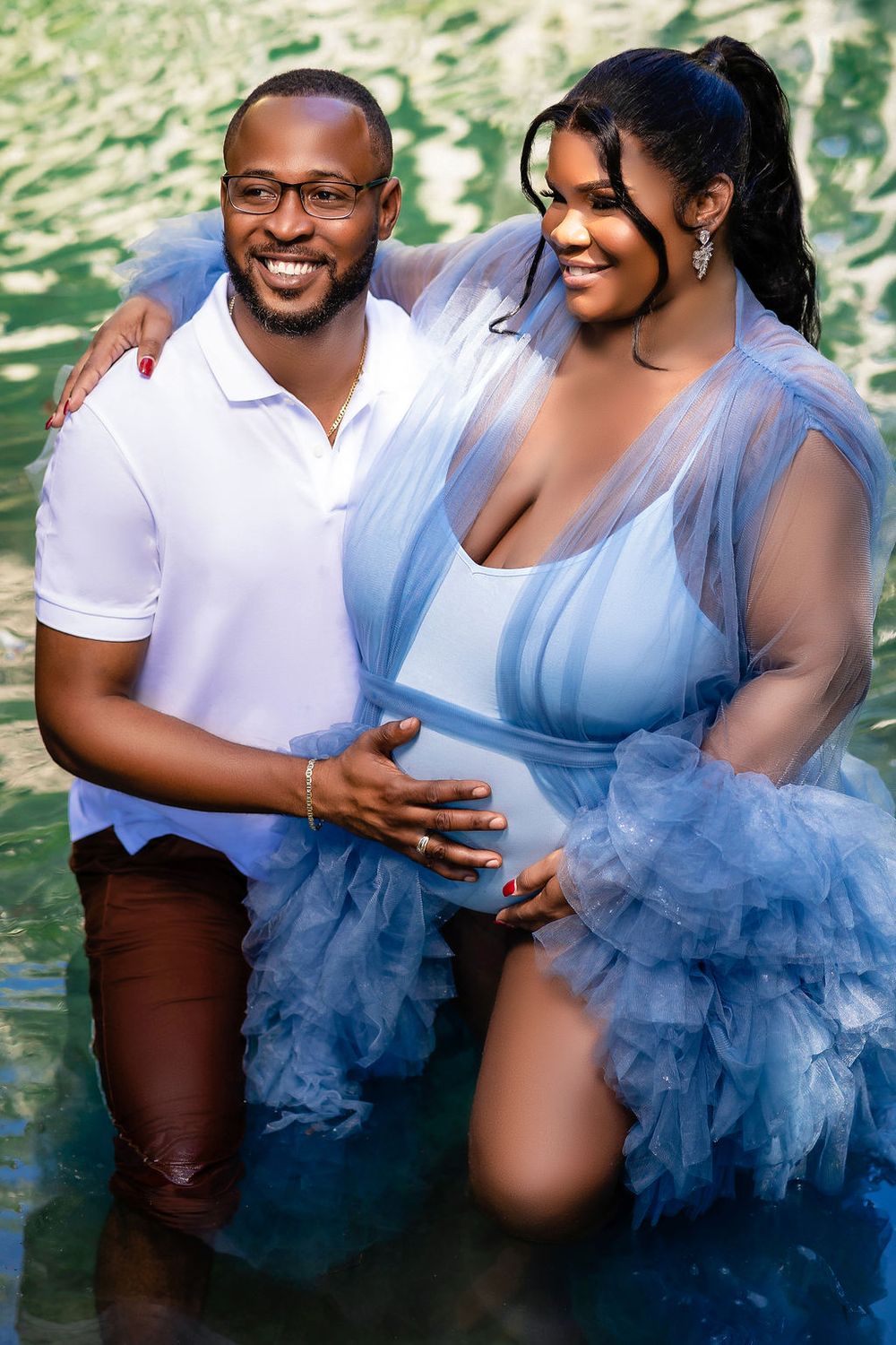 Expecting couple standing in the turquoise water, her blue tulle floating around them