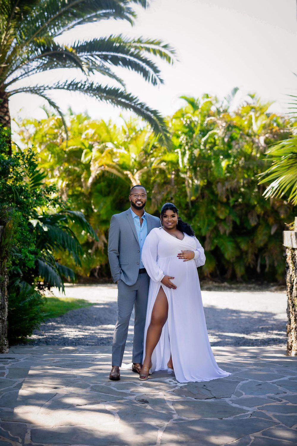 Expecting couple on a sunlit garden path lined with palms