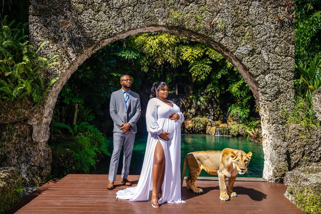 Expectant mother in a white gown beneath a coral arch above the lagoon