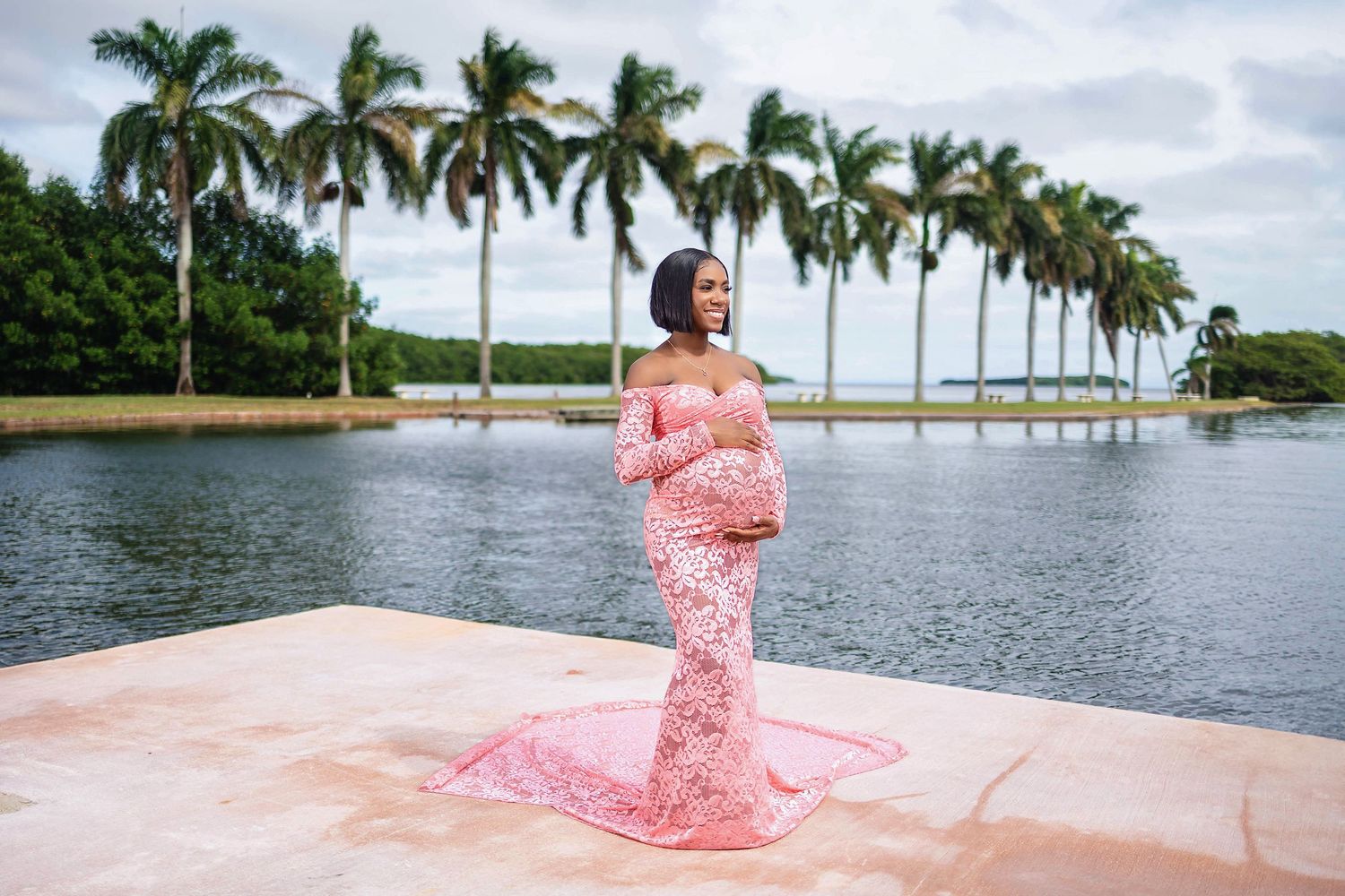 Expecting mother in a pink gown standing beneath royal palms on a South Florida estate lawn