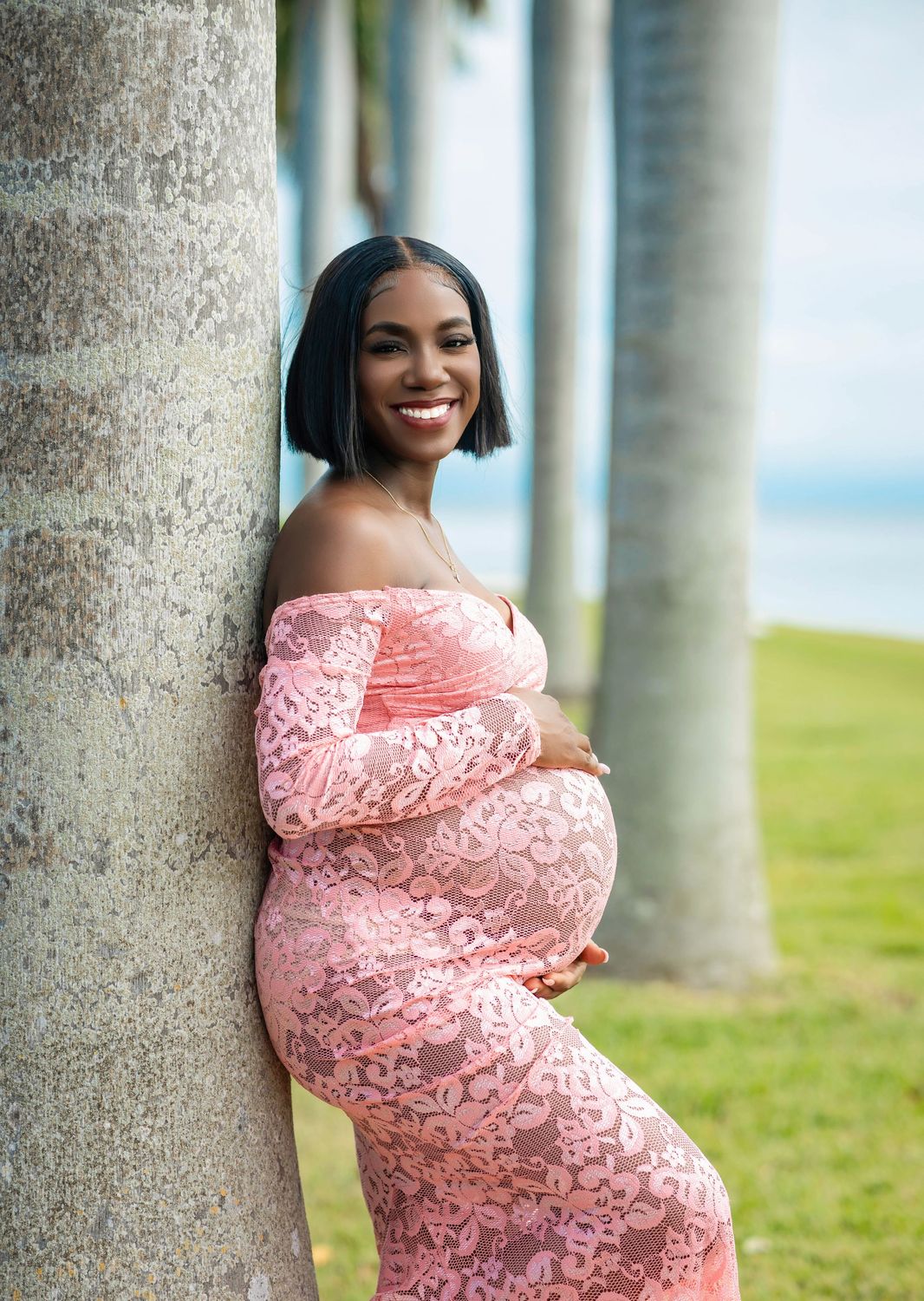 Maternity portrait in a blush sequin gown leaning against a palm trunk