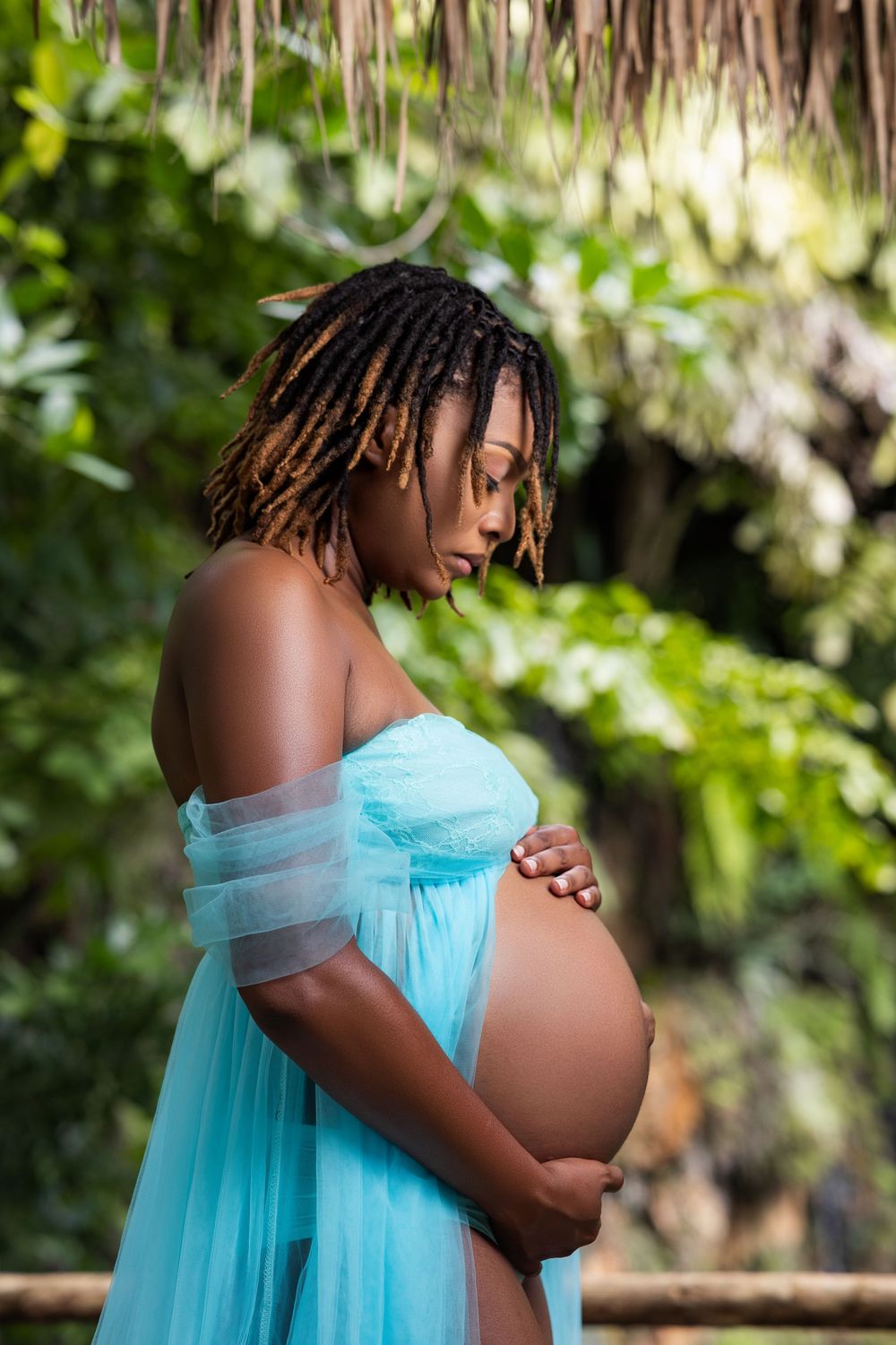 Profile maternity portrait in blue tulle among tropical ferns