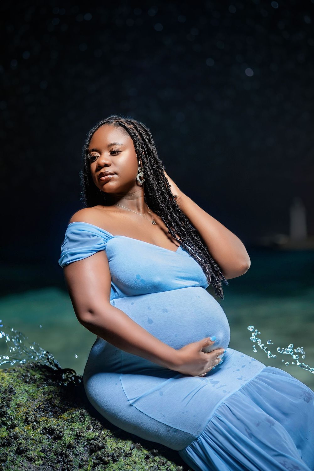 Expectant mother in a powder blue gown on the rocks above the ocean