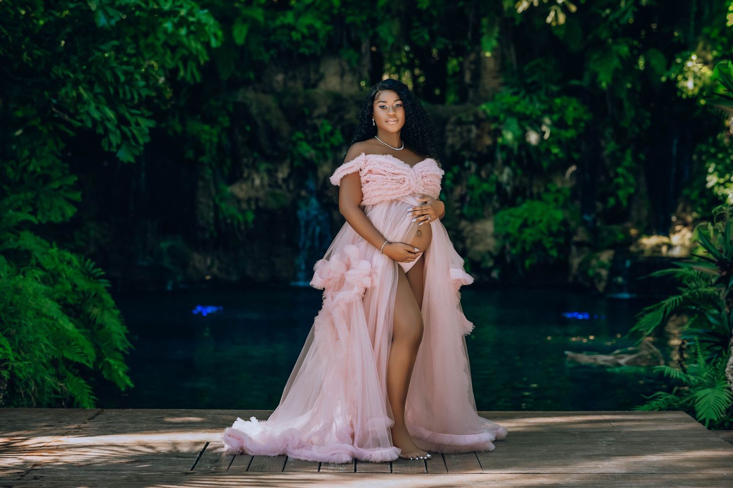 Mother to be in a blush gown on a jungle path beside a blue spring