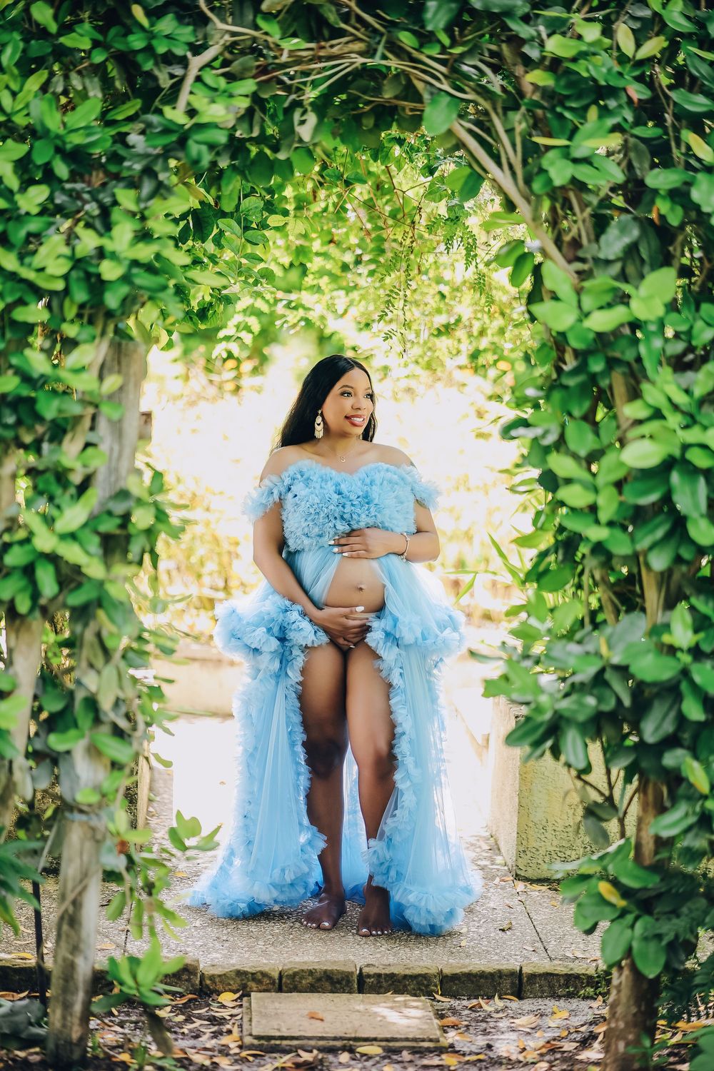 Maternity portrait in a blue gown framed by a climbing ivy arch