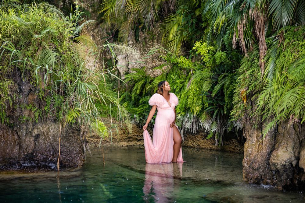 Mother to be in a blush gown wading in a clear tropical spring