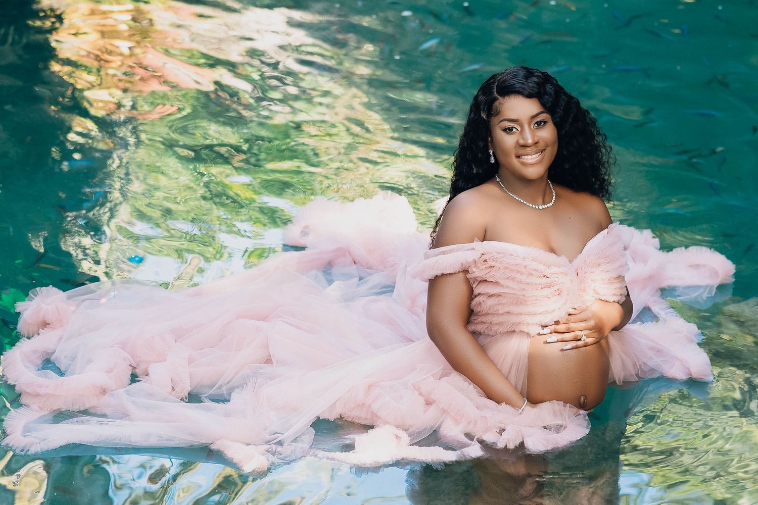 Mother to be in blush tulle reclining at the edge of a turquoise pool