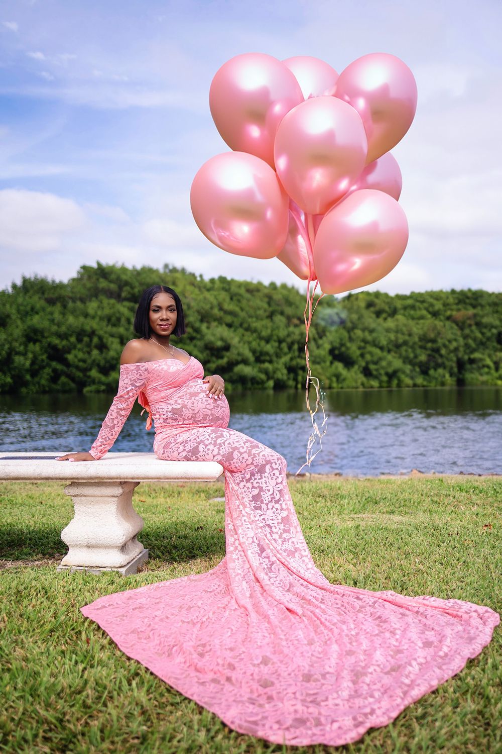 Maternity portrait in a pink lace gown with pink balloons on a lawn