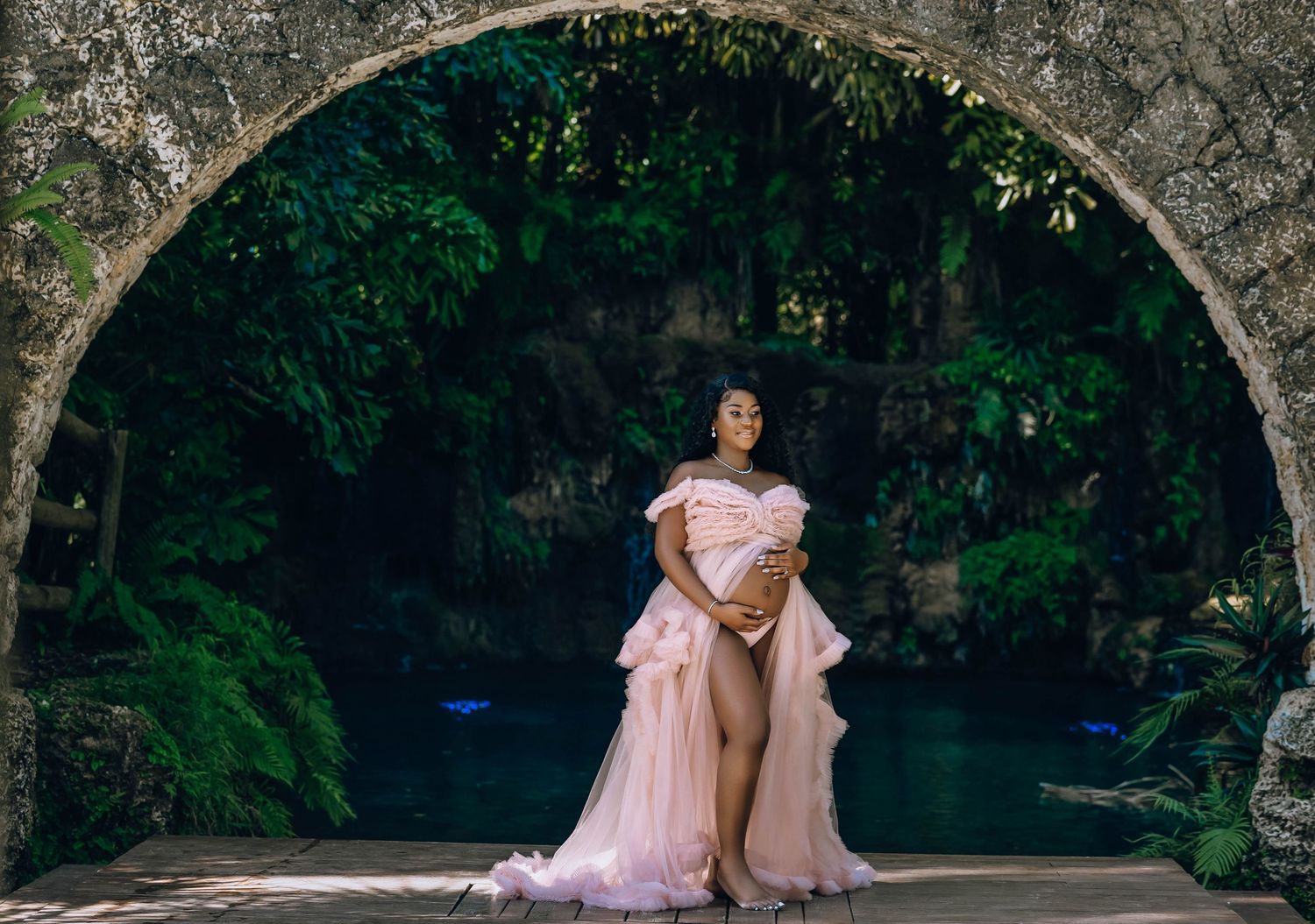 Mother to be in a blush gown beneath a coral stone arch
