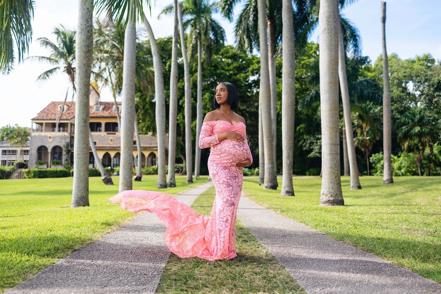 Expecting mother in a pink gown on a palm lined walkway at golden hour