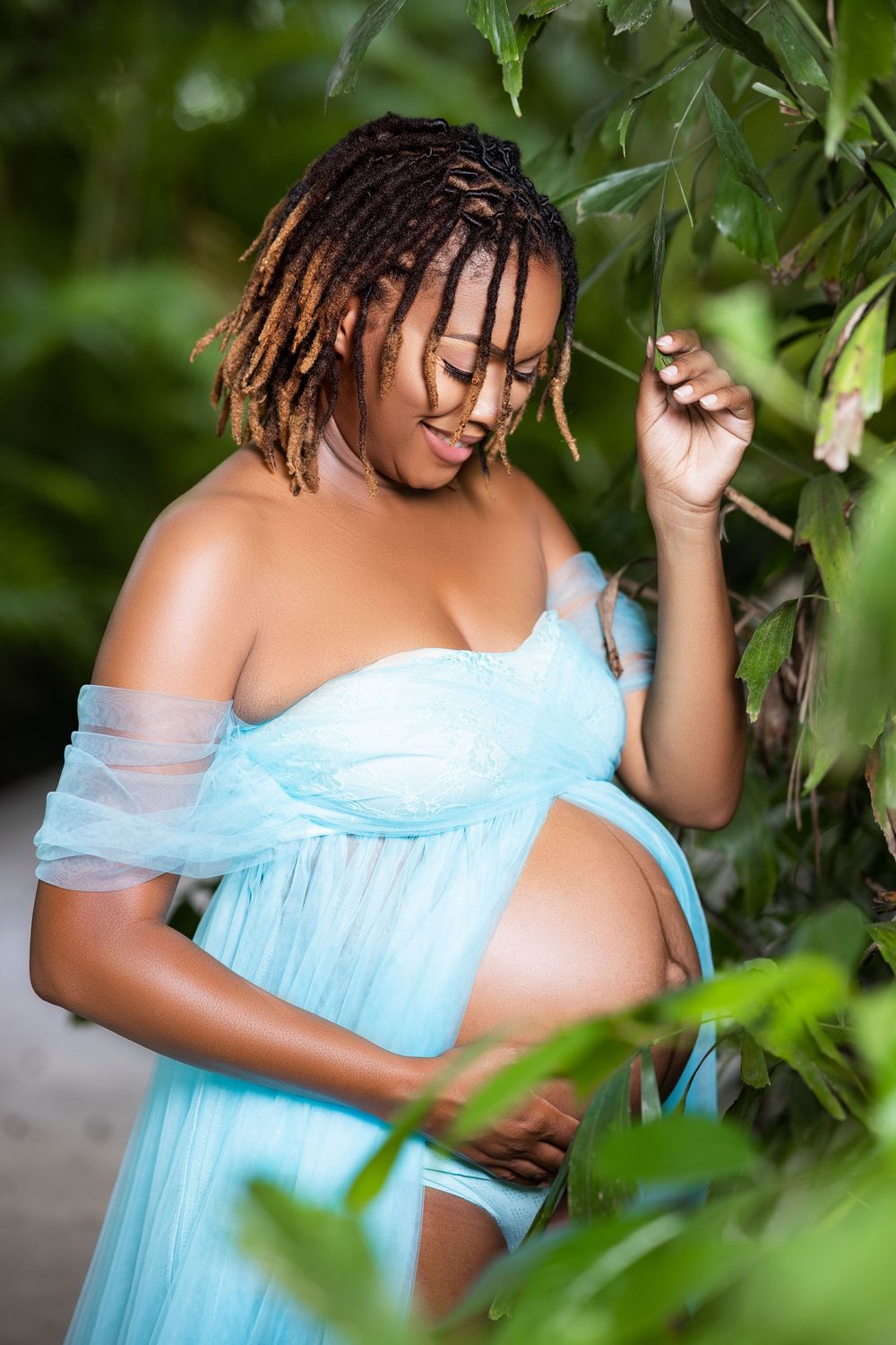 Mother to be in a blue tulle gown among tropical leaves