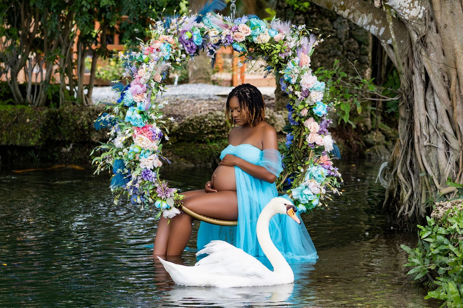 Maternity portrait in a blue gown on a floral arch over the water
