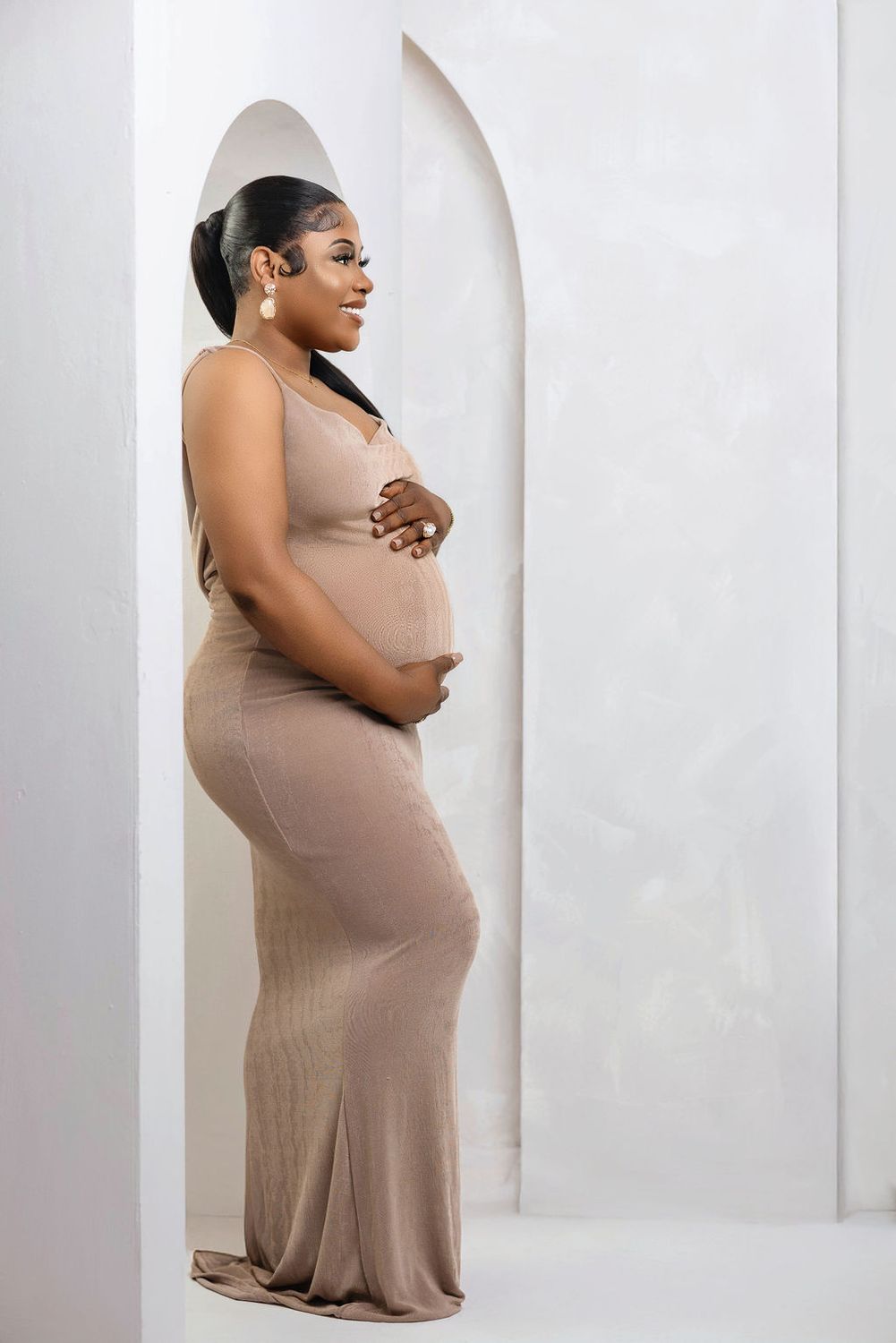 Expectant mother in a nude fitted gown, soft studio profile portrait
