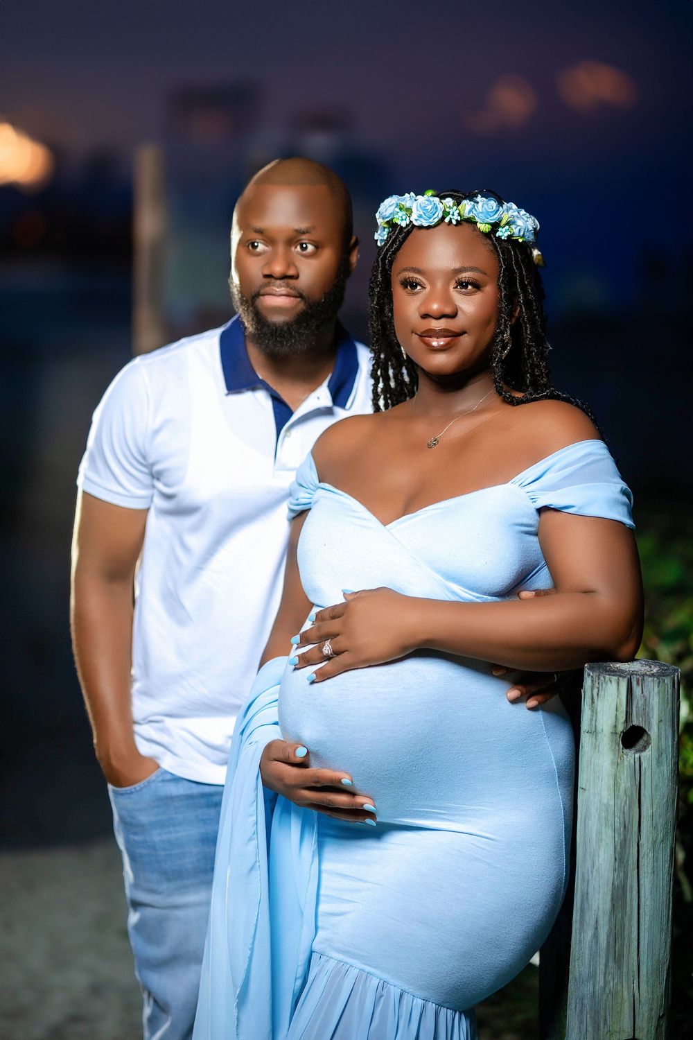 Expecting couple in blue and white holding her belly in a tropical garden