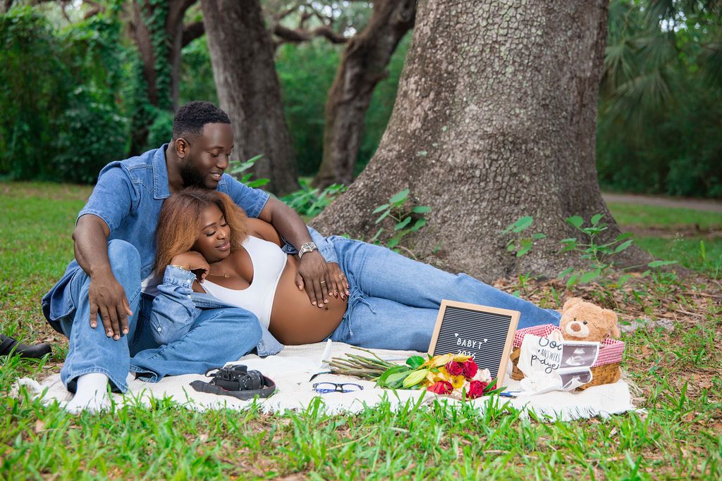 Expecting couple laughing together on a picnic blanket under live oaks
