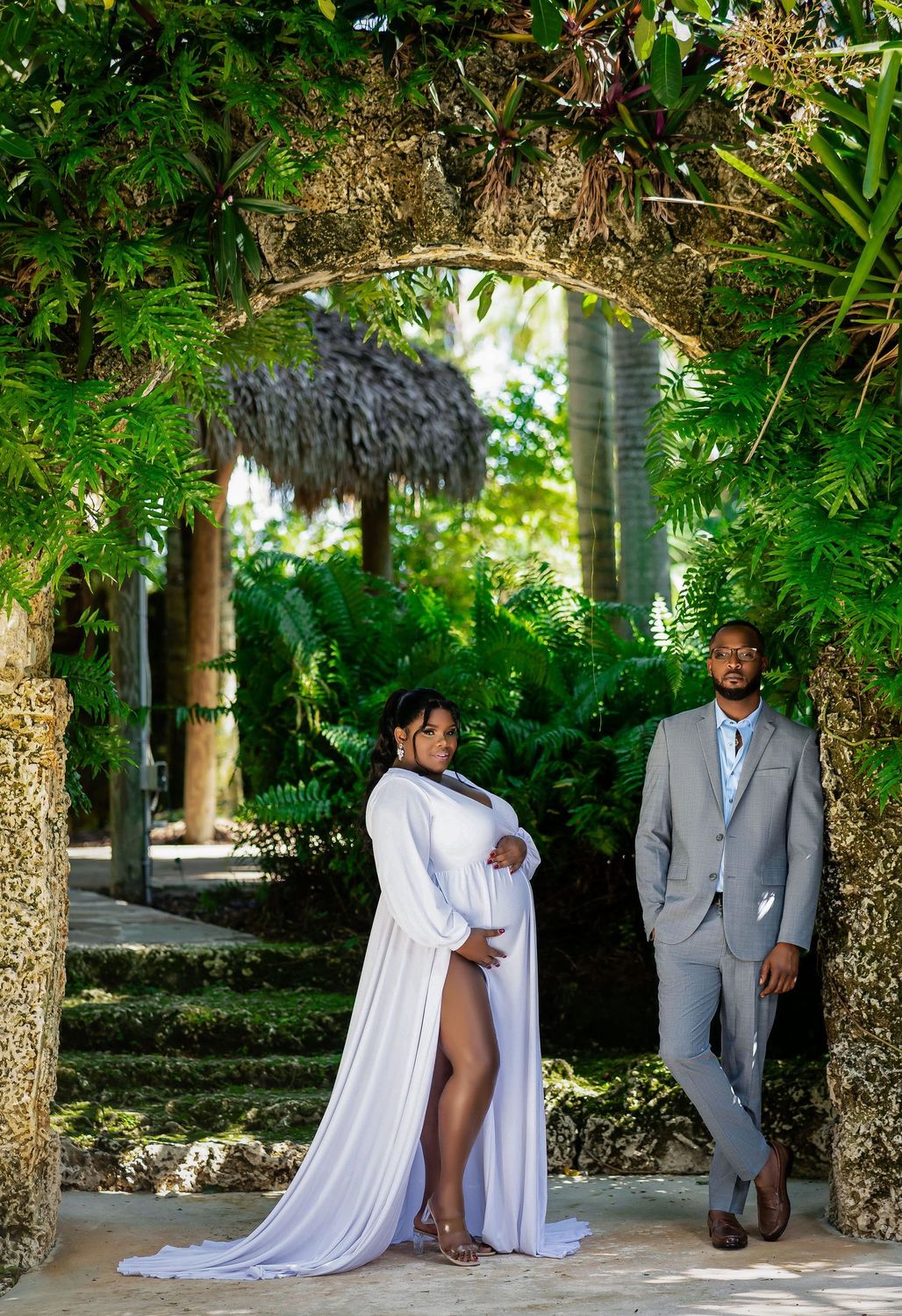 Expecting couple in white at a tropical garden pavilion