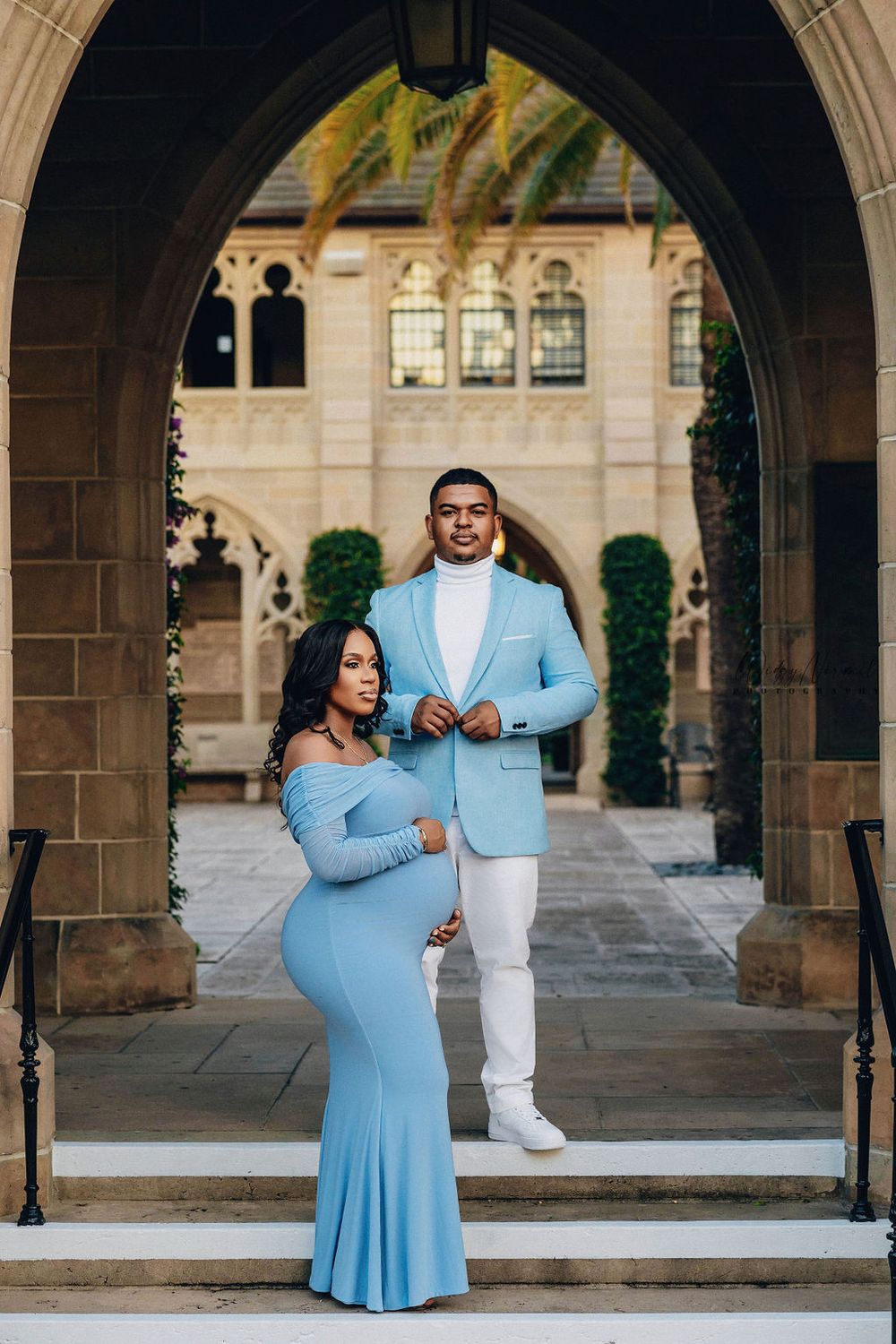Expecting couple in blue beneath a stone archway