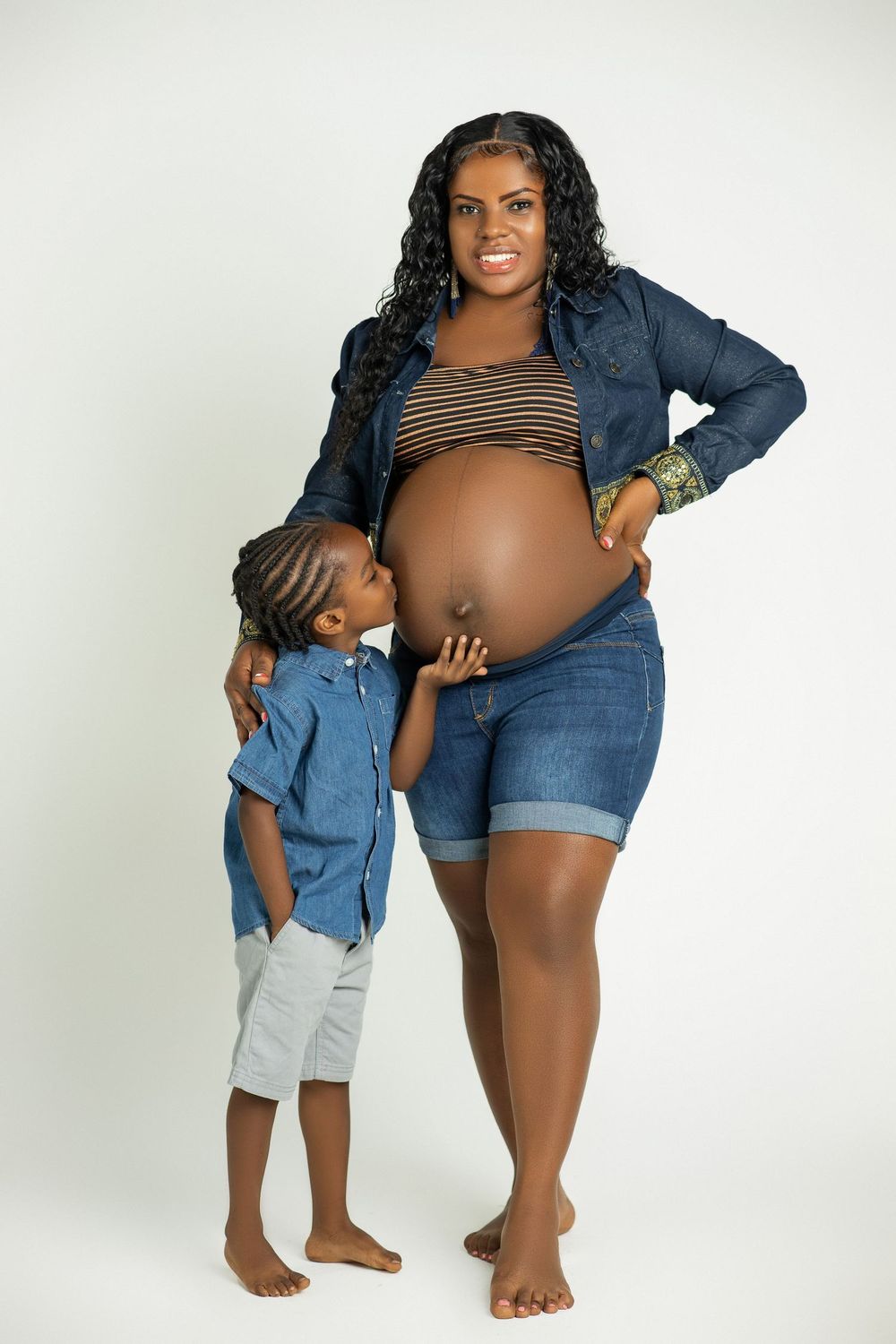 Expectant mother in denim with her young son holding her belly