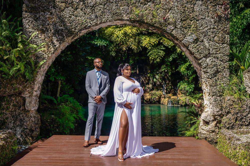 Expecting couple in white framed by a coral stone arch