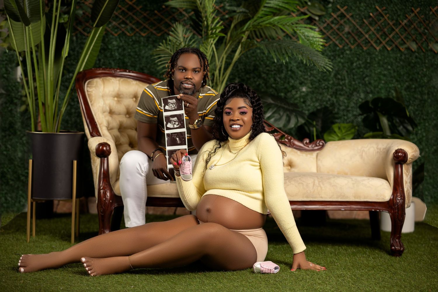 Couple on a vintage sofa with greenery, holding an ultrasound photo