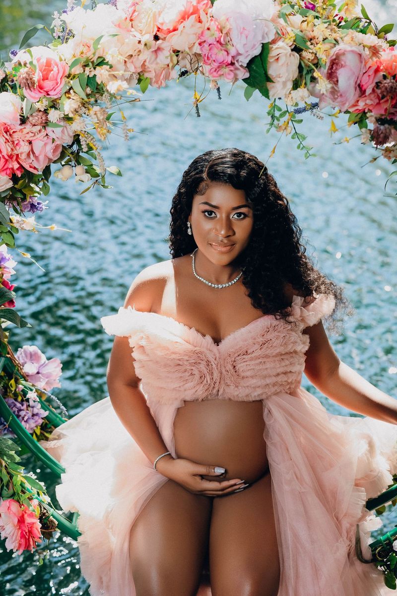 Expectant mother in a blush gown surrounded by flowers at a South Florida garden