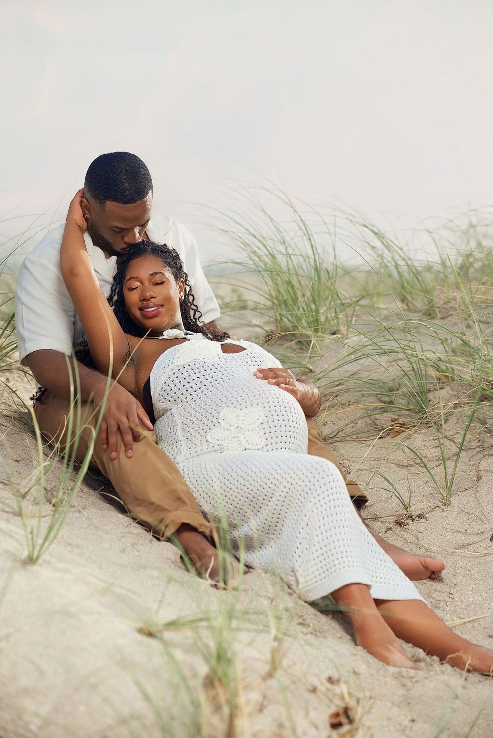 Expecting couple resting together in the dune grass at sunset